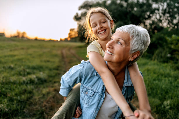 grandmother carrying her granddaughter on back outdoors - neto imagens e fotografias de stock