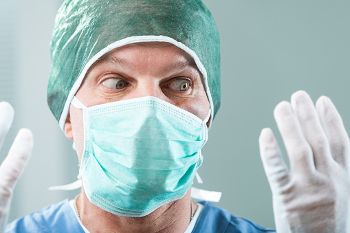 Close-up of a surgeon, noticing something amiss with his gloves. Individual expertise can falter when provided subpar equipment. Blame remains ambiguous, but insurance could help