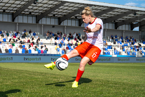 Female football player kicking ball while playing match on football pitch.