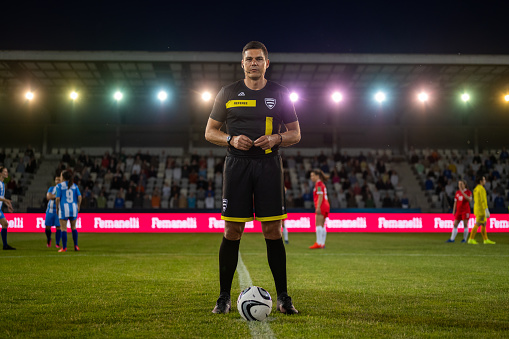 Portrait of smiling mature referee standing on football pitch during toss.