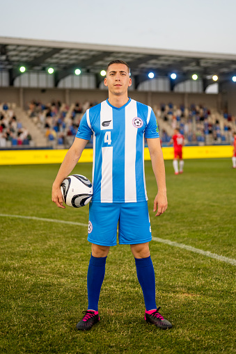 Portrait of male football player standing with football on football pitch.