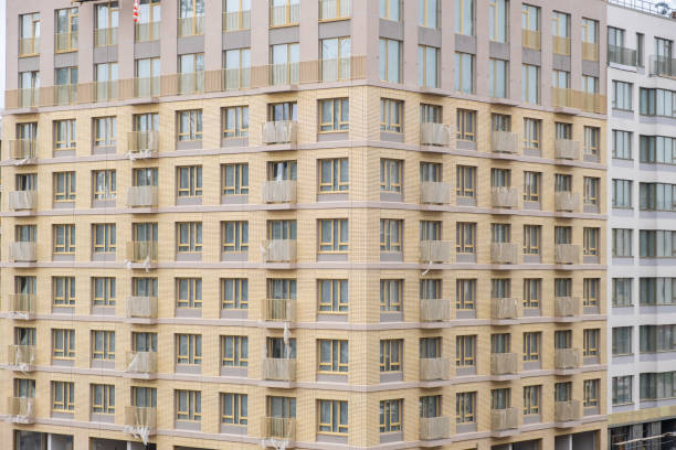New, high built residential building with balconies and windows. Builders work on large construction sites, and there are many cranes working in the field of new construction.