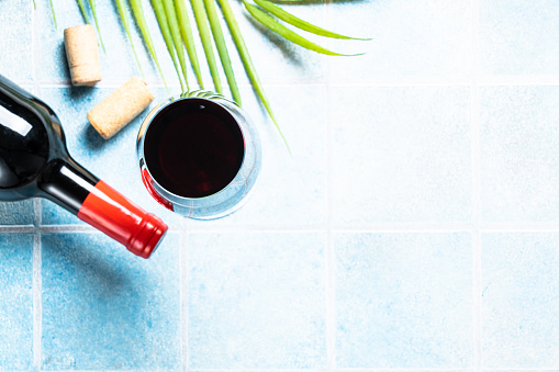 Red wine on blue background. Glass wine with bottle and palm leaves. Flat lay image with copy space.