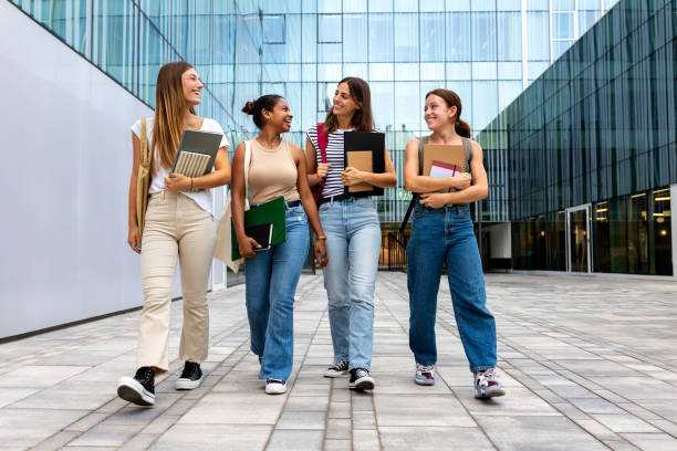 Multiracial happy female university students walking to class together while talking. Young people in college campus.