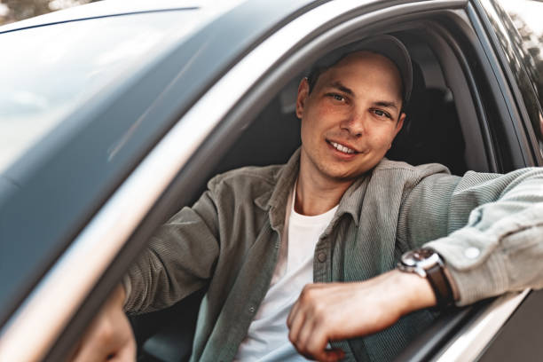 istock Young smiling man sitting in a car with open window 1637781323