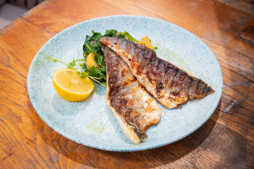 Grilled fish fillets served with boiled chard and potatoes in a plate on wooden restaurant table, fine dining healthy eating