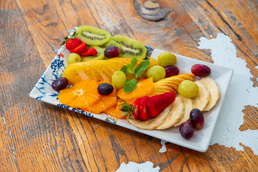 Tropical and continental fruit sliced and offered on rectangular tray in fine dining, wooden table