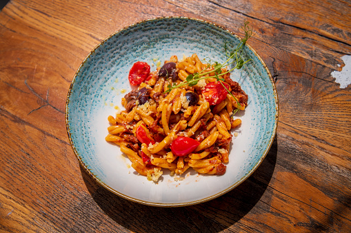 Tasty appetizer plate served on restaurant table, pasta fusilli, cherry tomatoes, black olives and ground beef in tomato sauce, fine dining Mediterranean style