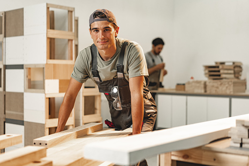 Portrait of young male carpenter standing in the wood workshop close up