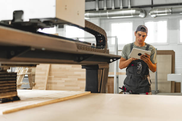 istock Young carpenter operating machine for wood processing at a furniture factory 1637795757
