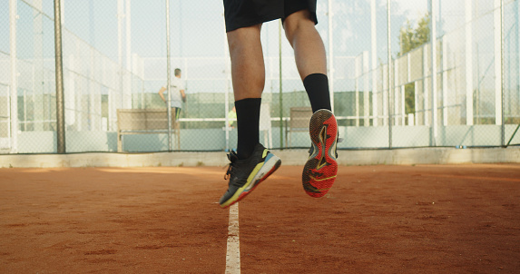 Detail of a tennis player's feet while he's jumping to serve at clay court. Human body part close up detail.