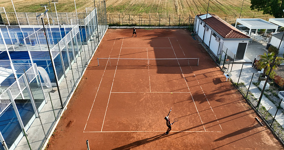 Aerial view of a tennis player during a match. Drone shot from behind a player, aerial view. Orange tennis court field.