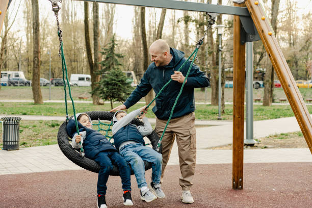 Father swinging his two little sons on a swing on playground in park