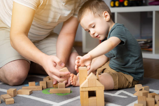 mały chłopiec 2,5 roku gra z tatą w drewniane klocki. spędzanie czasu z dziećmi. zajęcia edukacyjne dla dzieci. pokój dziecięcy. pomieszczeniach. selektywne ustawianie ostrości - caucasian pensive male young adult zdjęcia i obrazy z banku zdjęć