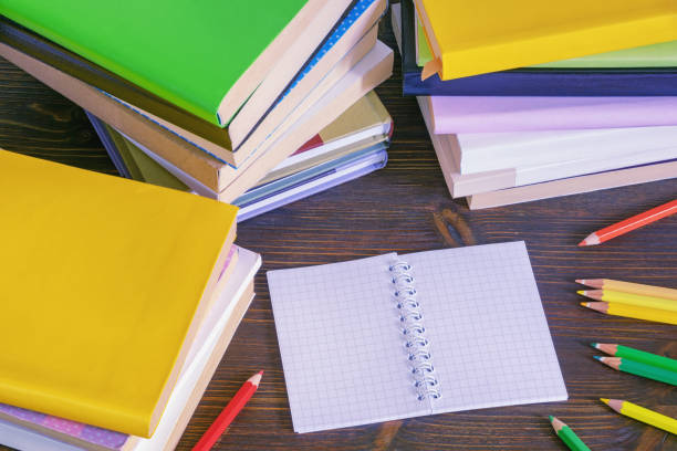 istock Stacks of different multicolored books, open notepad and pencils on dark rustic table. Copy space 1637839149