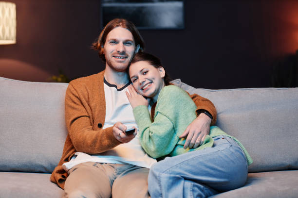 istock Smiling young couple watching TV at home and embracing 1637842053