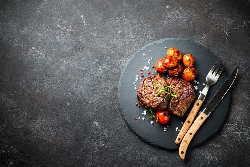 Meat steaks with vegetables and herbs at black background. Top view image with copy space.