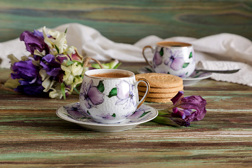 A cup with morning, brewed coffee, biscuits and a romantic bunch of wildflowers (irises) on a wooden table close-up