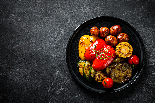 Grilled vegetables at black background. Potato, paprika, zucchini, eggplants and tomato. Barbecue dish, vegetarian. Top view with copy space.