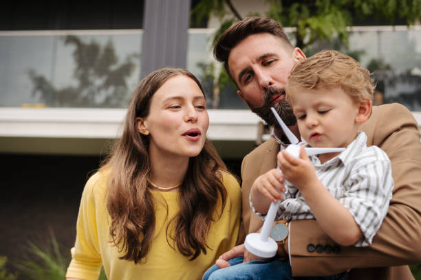 istock Smiling parents with little son blowing on wind turbine model. 1637850584