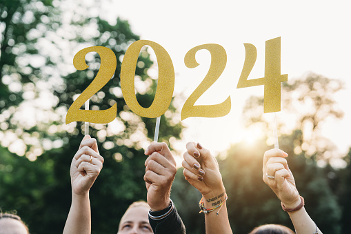 Friends are holding 2024 text to celebrate the New Year. Sunset outdoor. New Year's Eve concept.