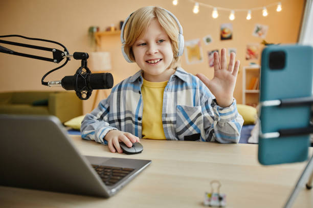istock Smiling boy waving hand to online audience while making livestream 1637874018