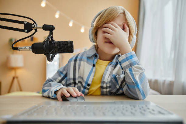 istock Upset little boy covering his face with hand while sitting in front of computer 1637874020