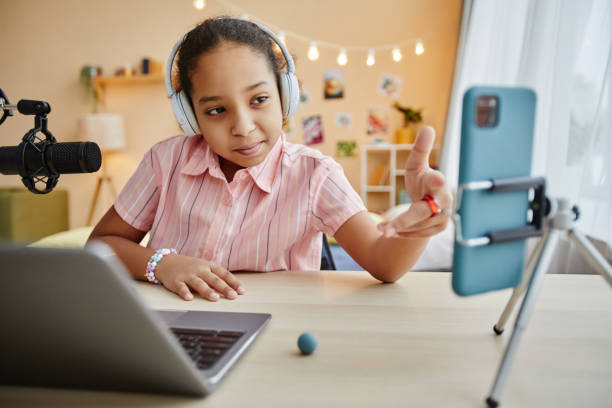 istock Cute schoolgirl pointing at smartphone screen while sitting by desk 1637874039