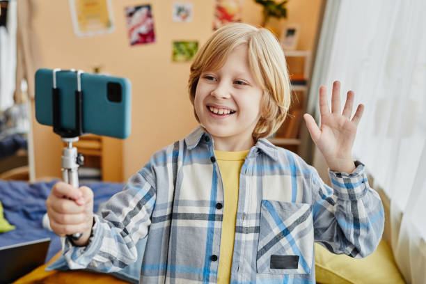 istock Smiling schoolboy waving hand to online audience while making livestream 1637874567
