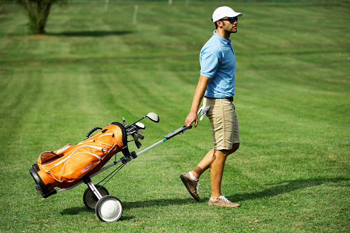 Closeup side view of a young man walking to the driving range at a golf course.