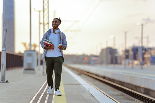 Smiling male student holding books. He is waiting for a train on the train station