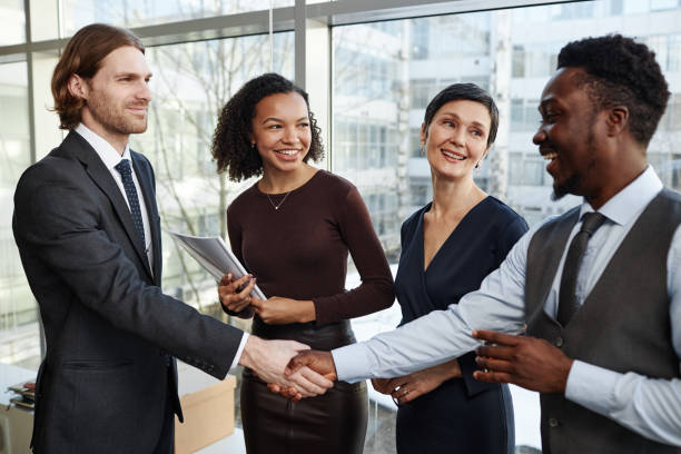 istock Smiling business partners shaking hands in office standing with drinks 1637890229