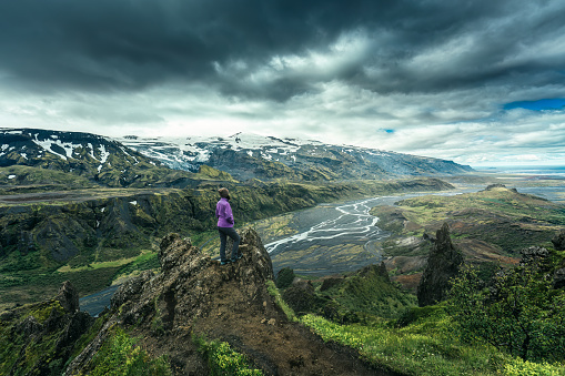 Dramatic volcanic landscape of Valahnukur trail and hiker woman standing in Thorsmork valley and moody sky in summer at Highlands of Iceland