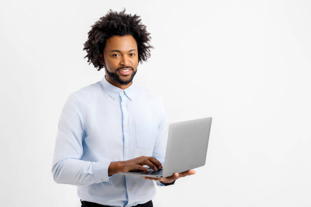 istock Smiling african businessman using laptop, standing at white backdrop, checking home finance, happy man looking at invoice 1637937879