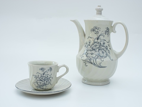 a ceramic old set of two cups and a teapot with a colored pattern stand on a gray table on a green background