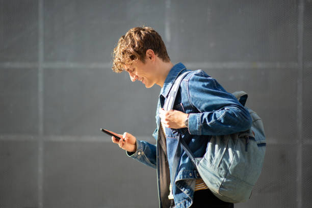 Smiling young man with bag using mobile phone outside