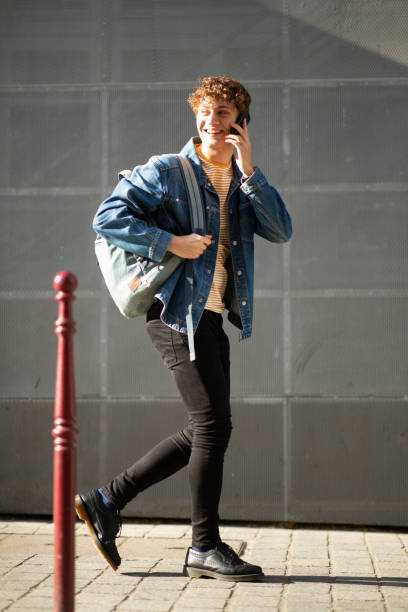 istock Happy young man walking and talking on mobile phone on sidewalk 1637959485