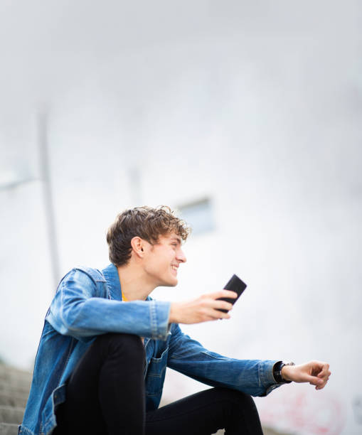 istock Smiling young man sitting outside with cellphone 1637959489