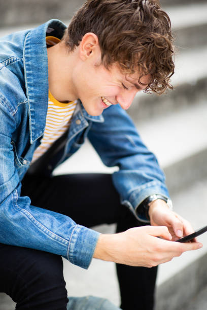 istock Smiling happy young man sitting outside and using cellphone 1637959493