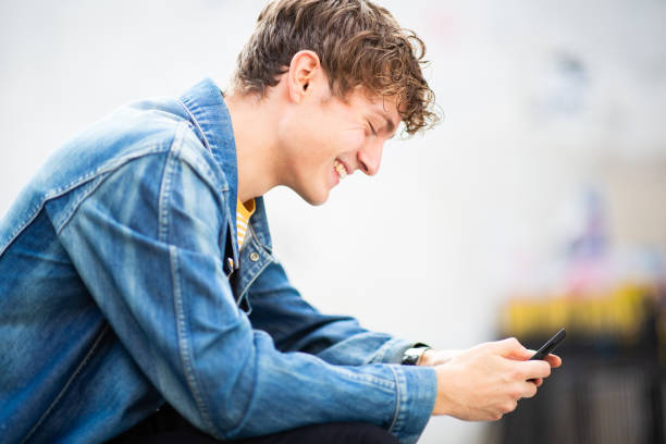 istock Smiling young man sitting outside looking at cellphone 1637959495
