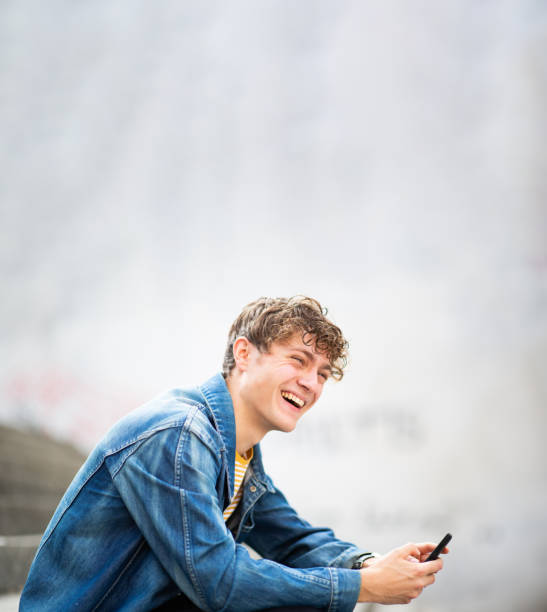 istock Young man with phone looking away and laughing outside 1637959496