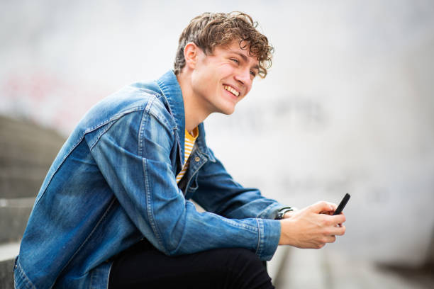 Smiling young man sitting outside with mobile phone