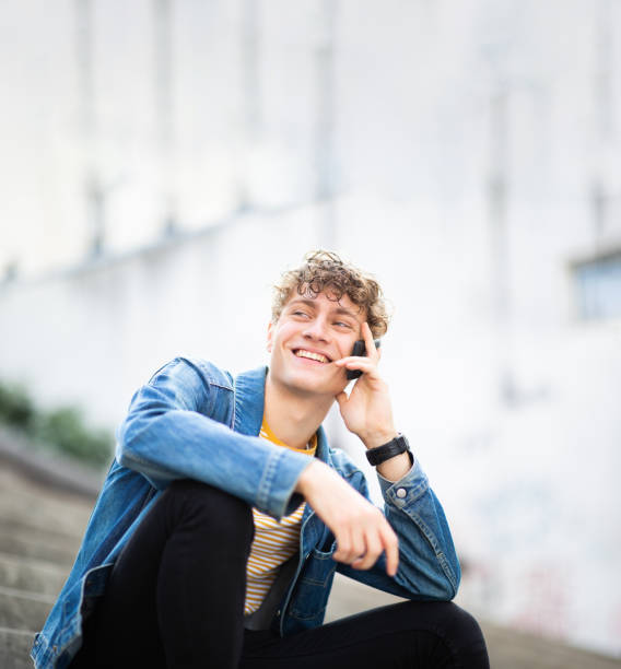 istock Happy young guy sitting outside and talking on mobile phone 1637959504