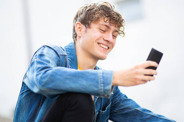 istock Smiling young man sitting outside and looking at mobile phone 1637959506