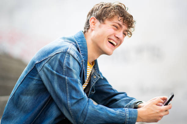 istock Laughing young man sitting outside with mobile phone 1637959515