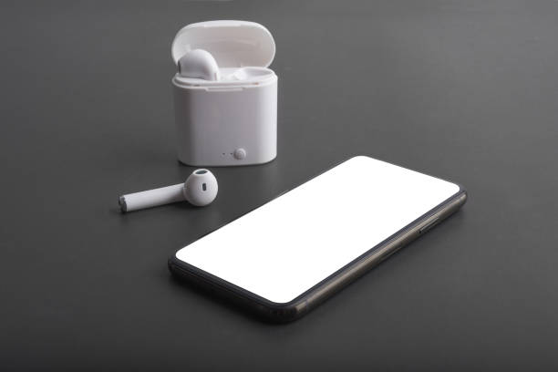 Simple composition of a mobile phone and wireless headphones on black surface.