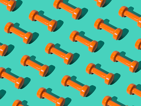 Creative pattern composition made of orange dumbbells on pastel green background. Minimal fitness, healthy lifestyle and sport concept. Trendy exercise and fitness backround idea.