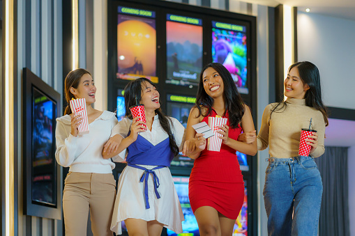 Diverse friends, popcorn in hand, stroll joyfully in front of the cinema, embodying friendship and fun-filled anticipation for an entertaining movie night.