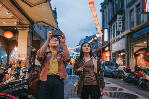 Asian Chinese female tourist photographing Old Town with smart phone in Taipei City