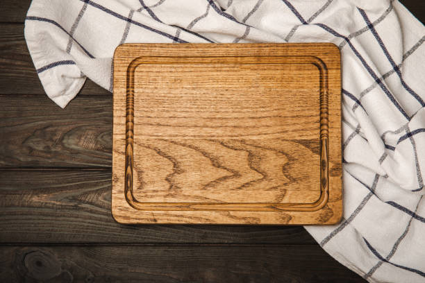 istock Cutting board over towel on wooden kitchen table. Cutting board and kitchen towel on brown textured background. Menu food card or recipes background concept.MOCKUP. Design. Place for text, copy space. 1637994049